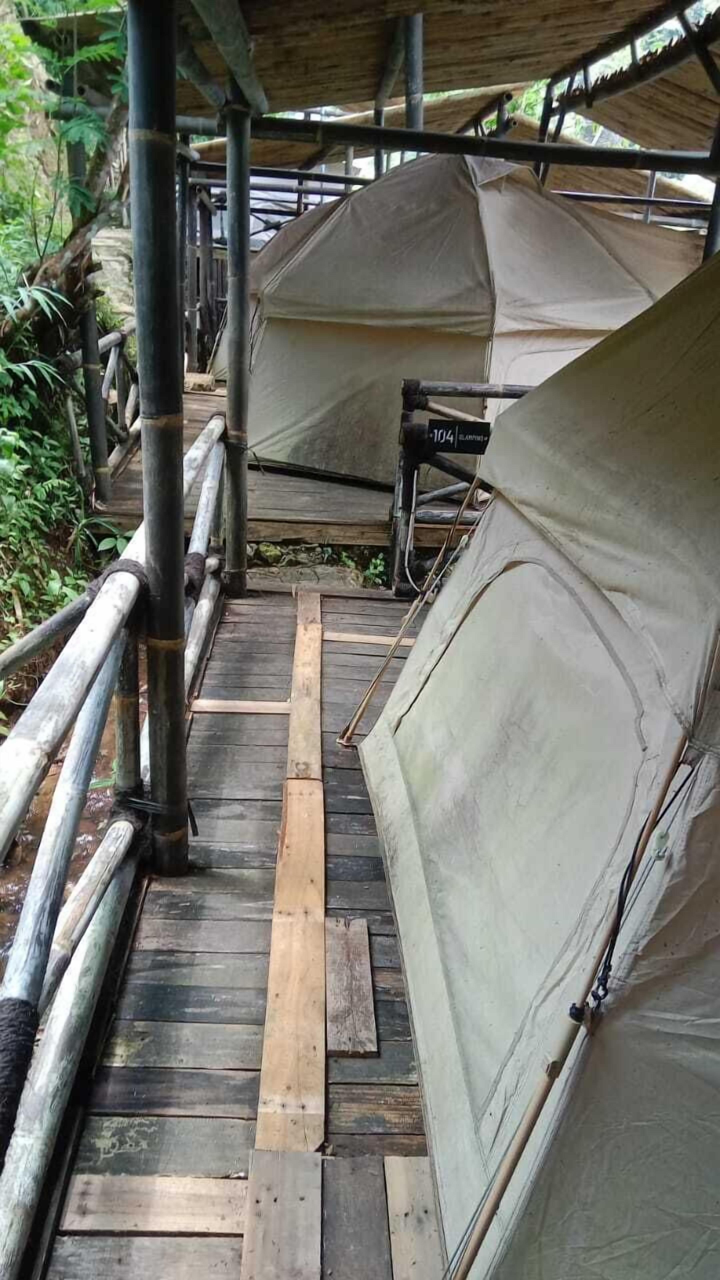 A covered wooden deck with metal railings, leading to a series of tents.