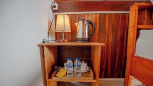 Una estantería de madera con un hervidor, una lámpara, dos botellas de agua, una taza y una bandeja con llaves y una tarjeta.