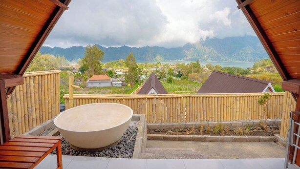 Una terraza de madera con una bañera grande, valla de bambú y vista a un paisaje montañoso.