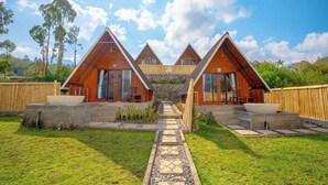 Un moderno alojamiento con tres cabañas de madera triangulares, cada una con un sendero de piedra que conduce a una estructura central de piedra.