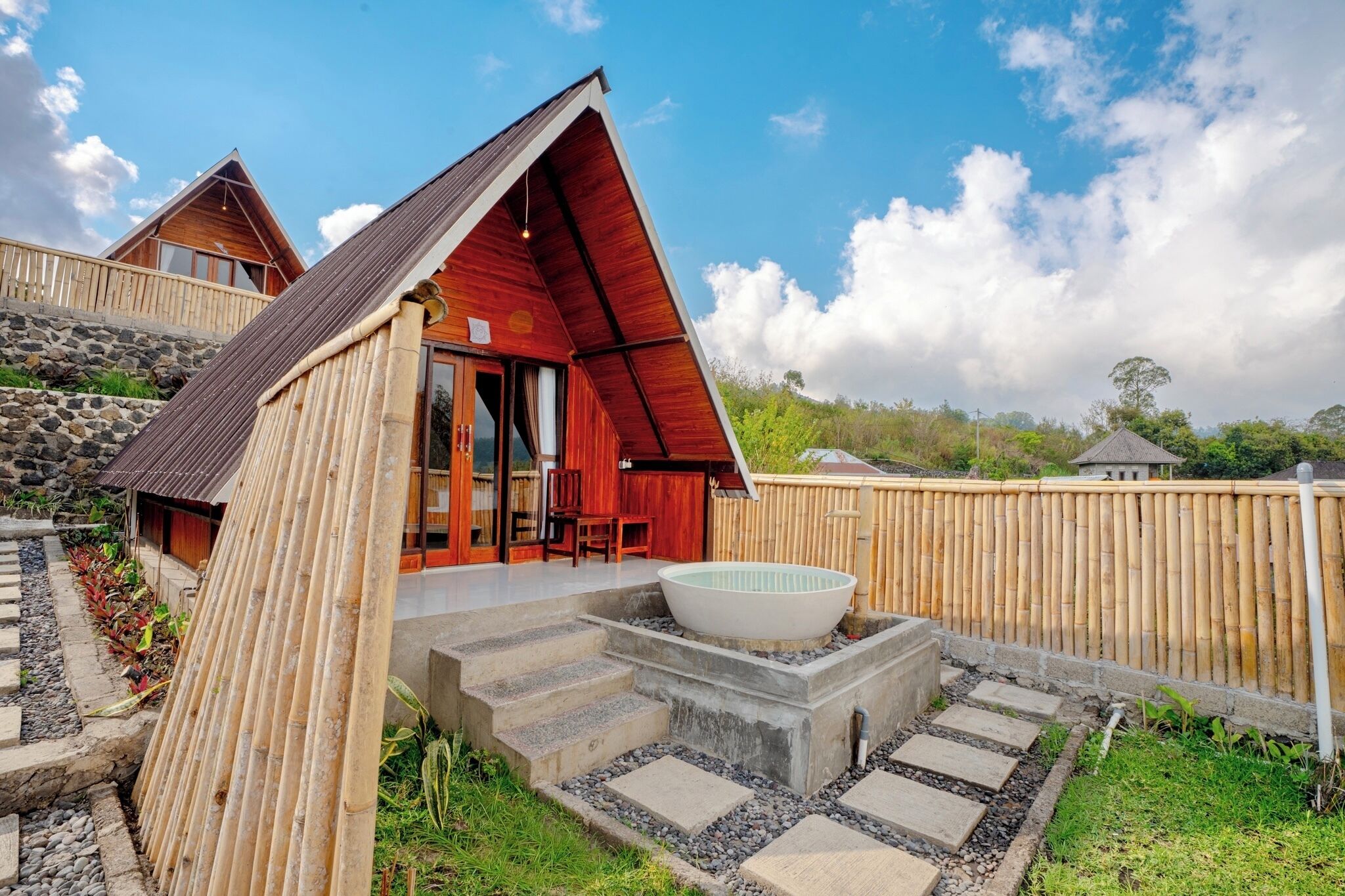 Une maison moderne avec un toit rouge, un grand espace extérieur aménagé pour se détendre et un chemin de pierre menant à un jacuzzi.