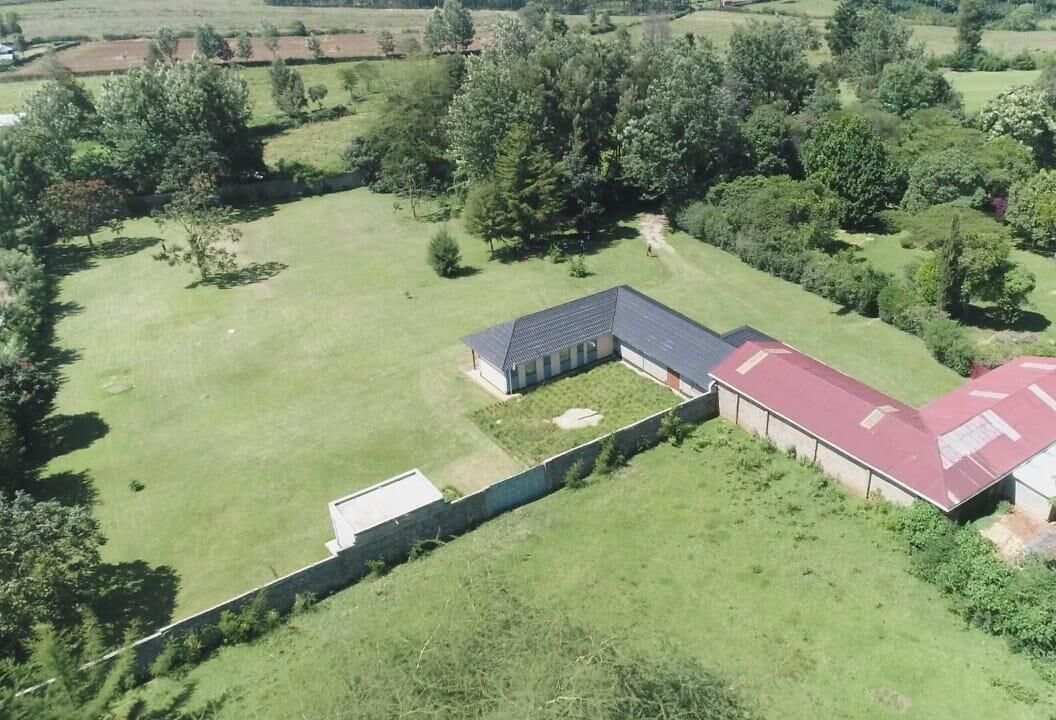 Vista aérea de una propiedad con un amplio espacio verde, un edificio de techo rojo y una estructura más pequeña con techo oscuro.