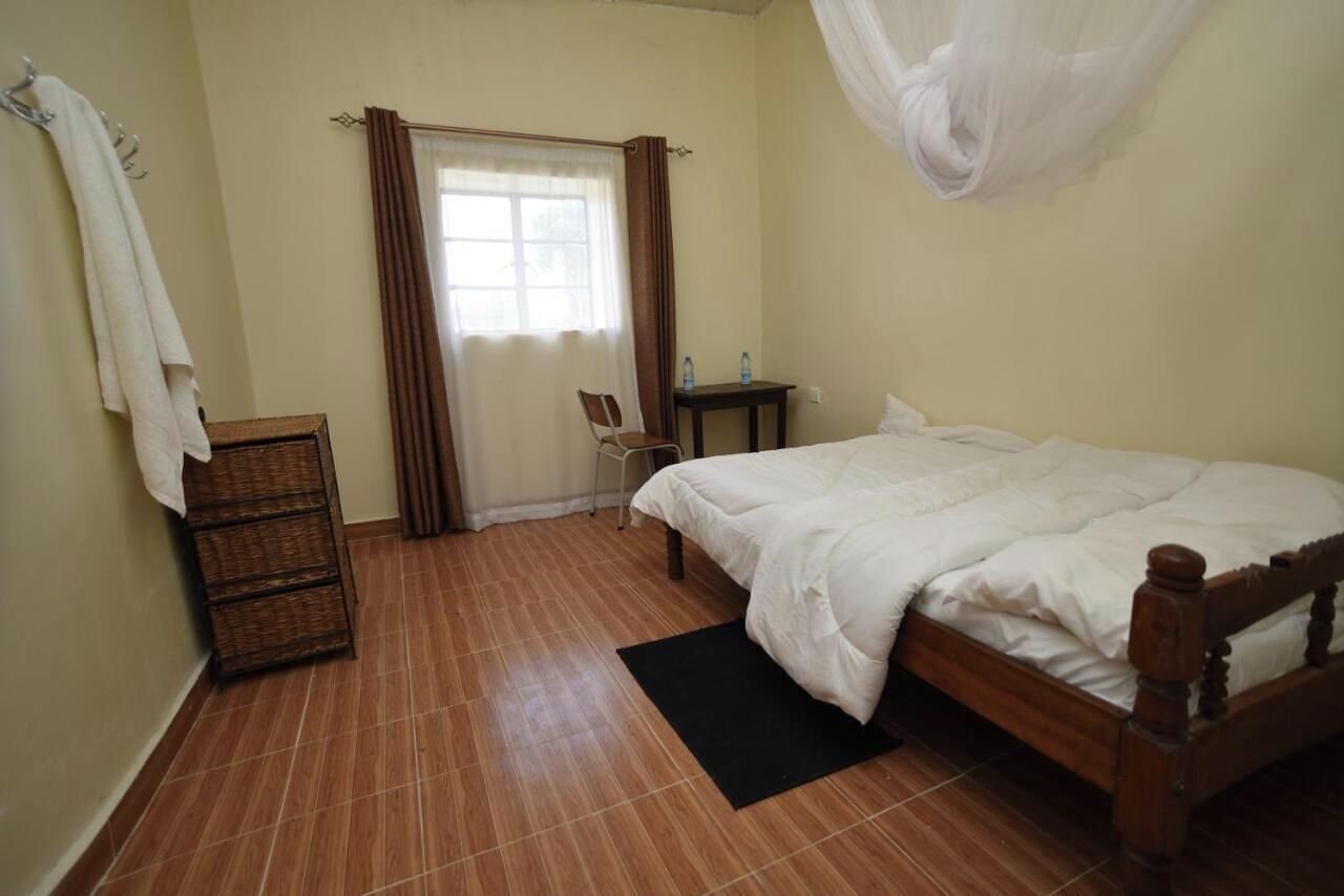 A bedroom with a wooden bed, a small desk, a chair, a wicker chest of drawers, and a window with curtains.