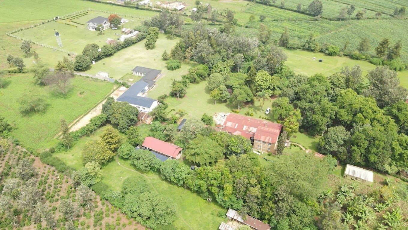 An aerial view of a rural property with multiple buildings, green fields, and scattered trees.
