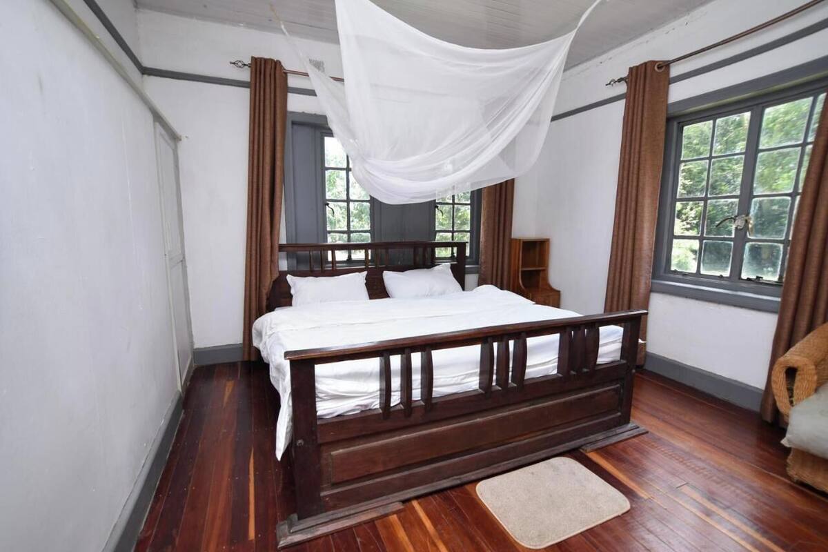 A bedroom with a wooden bed, white bedding, and a window with curtains.