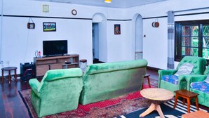 Un salón amplio con sofás verdes, un televisor y un tapete rojo con estampado.