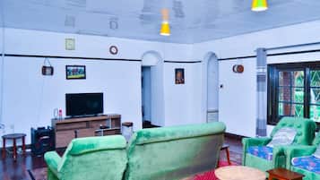 Un salón amplio con sofás verdes, un televisor y un tapete rojo con estampado.