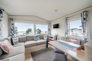A modern living room with a sofa, a dining table, and a TV mounted on the wall. - Cabin - Sleeps 4 - Pets Ok - Balcony - Parking (Watchet)