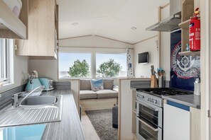 Una cocina compacta con estufa, lavamanos y ventana con vistas a la vegetación.