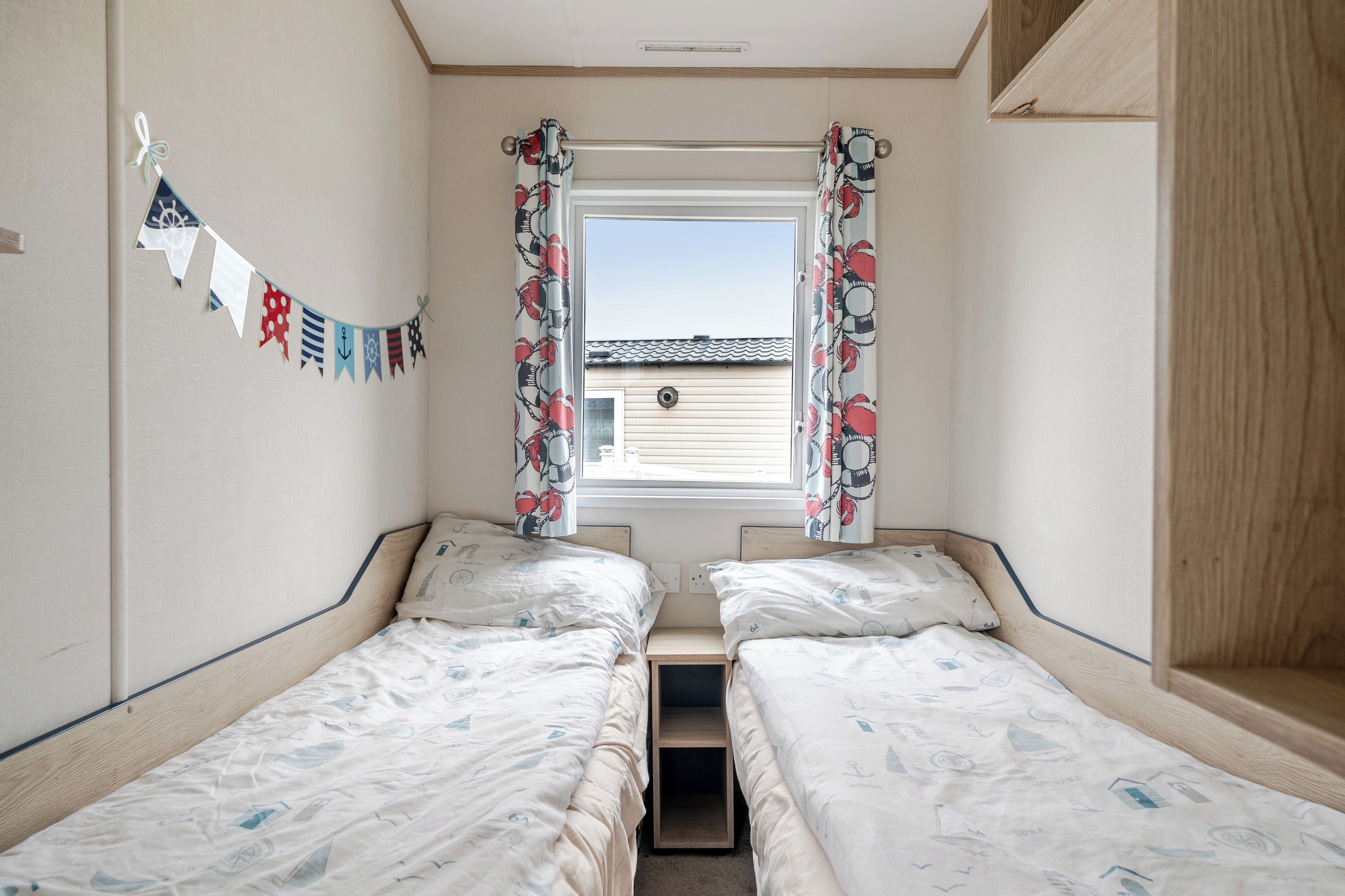 A room with two single beds, a window with curtains, a wall-mounted flag, and a view of a building outside.