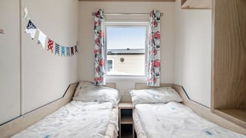 A room with two single beds, a window with curtains, a wall-mounted flag, and a view of a building outside.