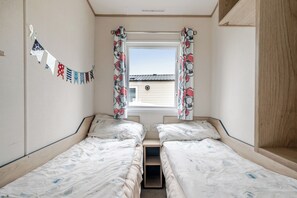 Una habitación con dos camas individuales, una ventana con cortinas, una bandera colgada en la pared y vista a un edificio.