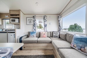 A compact living space with a kitchenette, a sofa set, and a view through a window. - Cabin - Sleeps 4 - Pets Ok - Balcony - Parking (Watchet)