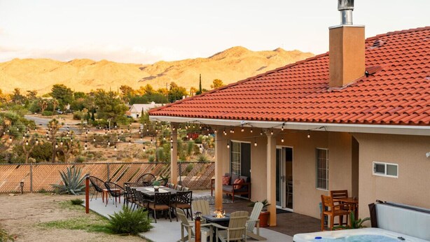 Una casa con techo de tejas rojas, un patio con mobiliario exterior y un jacuzzi.