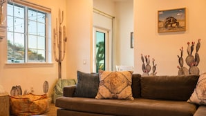 Un salón con un sofá marrón, cojines estampados, decoración de pared con cactus y un cuadro con temática de cactus.
