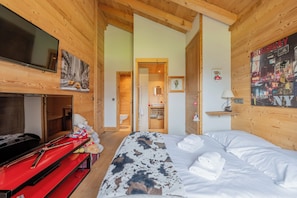 A hotel room with a wooden interior, a bed with a cowhide cover, a red fireplace, a television, and a poster of Broadway.