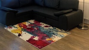 A modern living room with a black sectional sofa, a colorful rug, and pendant lighting. - 1 Bed Flat- Direct Links to Central London (Grays)
