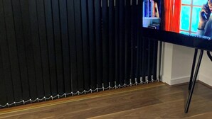 Een kamer met een houten vloer, een zwart gordijn en een televisie op een standaard.