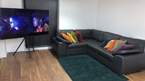 Een moderne woonkamer met een hoekbank, een flatscreen televisie en een groen vloerkleed.