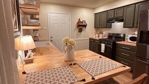 Una cucina compatta con mobili scuri, un forno a microonde, un forno e un lavandino. C'è un tavolo da pranzo in legno con sottopiatti e un vaso di fiori.