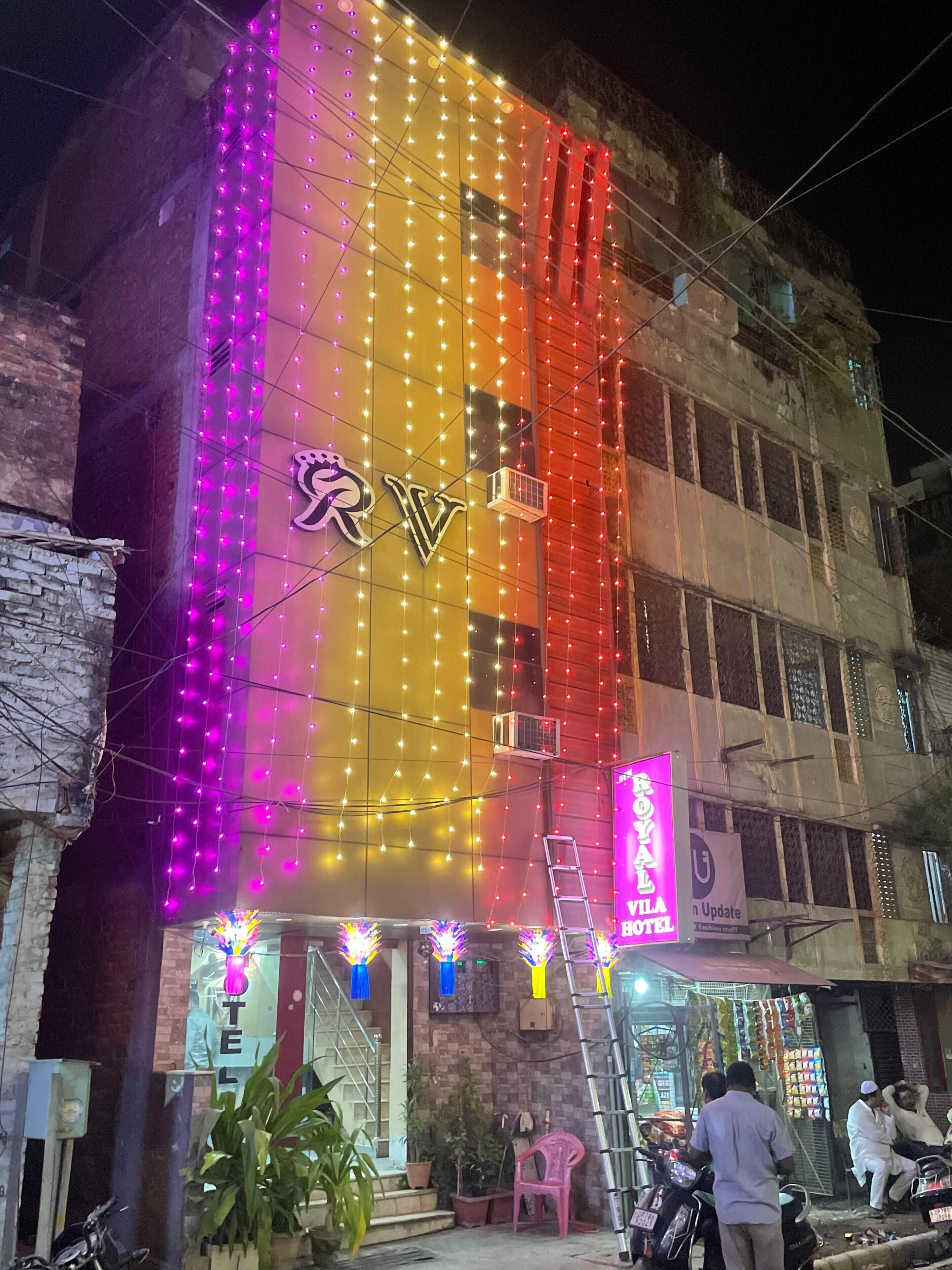 La façade d’un hôtel, avec une enseigne bien visible, un escalier et quelques plantes en pot.