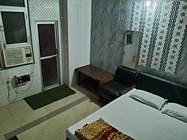 A hotel room with a bed, a desk, a chair, a small table, a bench, a window, and a door. - Hotel Yash Palace Kanpur (Kanpur)