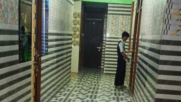 Un pasillo con baldosas blancas y negras estampadas, paredes verdes y una persona de pie cerca de una puerta.