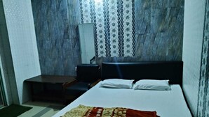 Una cama individual con una colcha estampada, una mesita de noche y una silla en una habitación con un papel tapiz decorado y un ventanal con cortinas.