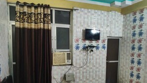 Una habitación con televisor montado en la pared, ventana con cortinas, aire acondicionado y una puerta.