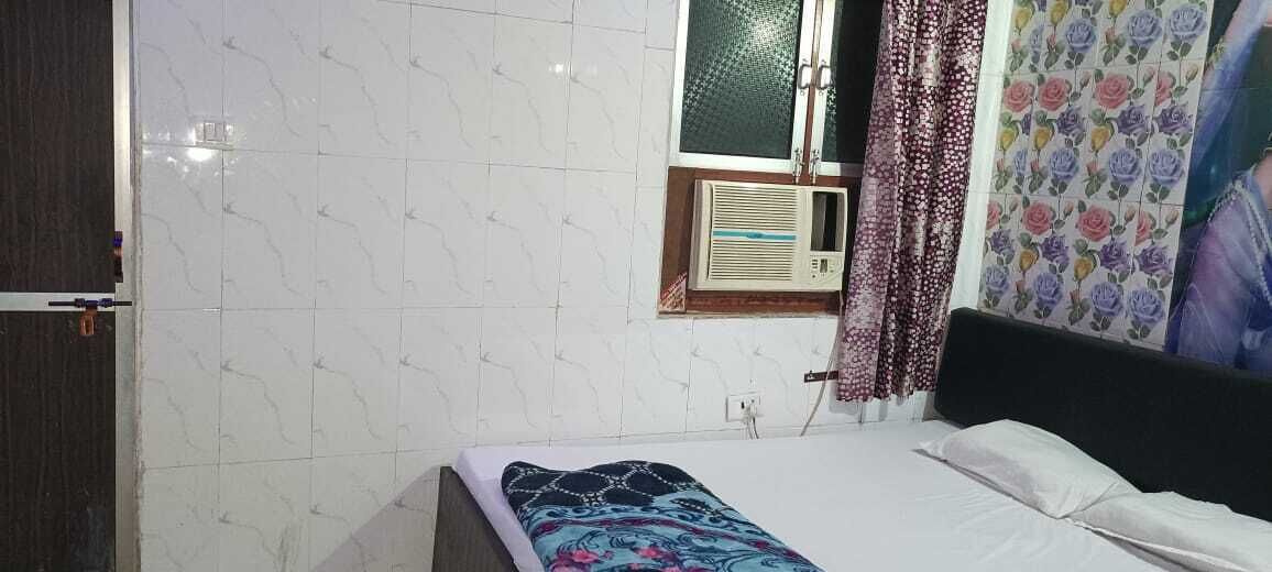 Un dormitorio con cama, ventana con cortina, aire acondicionado de pared y pared con azulejos.
