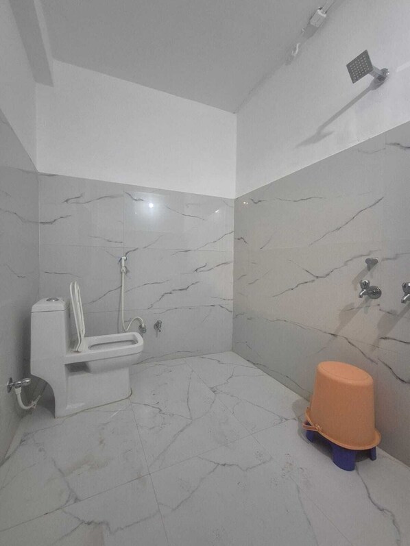 A bathroom with a toilet, shower, and a small orange stool. - Varun Hotel and Restaurant (Jaunpur)