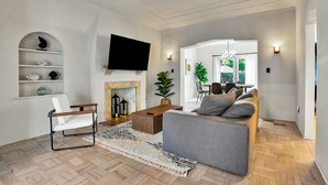 A modern living room with a sofa, a white chair, a fireplace, and a flat-screen TV. - Villa in the heart of design district! POOL+LOCATION (Miami)