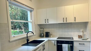 Een moderne keuken met witte kastjes, een ingebouwde oven, een vaatwasser en een raam met uitzicht op groen.