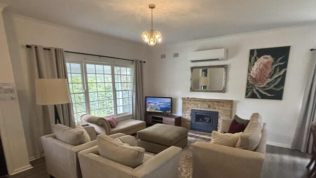 Een moderne woonkamer met twee beige banken, een flatscreen televisie, een open haard en een groot raam met gordijnen.
