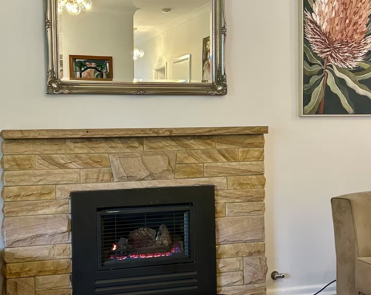 Una chimenea de piedra con una pantalla negra moderna, un espejo grande y ornamentado arriba y un cuadro floral a la derecha.