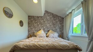 A bedroom with a bed, a bench, a window, and floral wallpaper. - Apartment at the Obersee (Bielefeld)