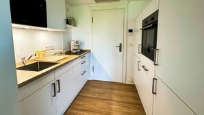 A compact kitchen with white cabinets, a wooden countertop, a built-in oven, and a coffee machine. - Apartment at the Obersee (Bielefeld)