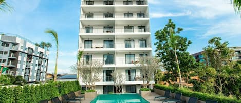 A multi-story hotel with a swimming pool, outdoor seating, and surrounding greenery.