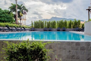 A swimming pool with lounge chairs, surrounded by greenery and a view of distant hills. - Sleek 2 Bed Apt T2-818 (Chalong)