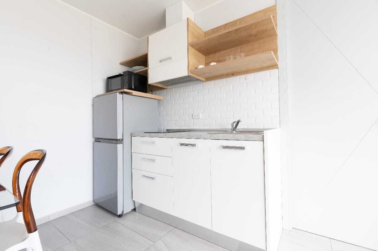 A compact kitchen with white cabinetry, a built-in microwave, and a wooden shelf above the stove.