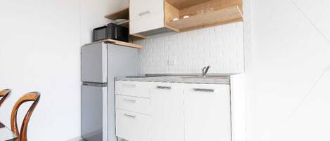 A compact kitchen with white cabinetry, a built-in microwave, and a wooden shelf above the stove.