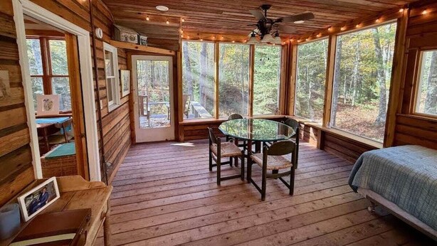 A cabin with a wooden interior, a round glass table, and a bed. - Tig Foster on Madeline Island (LaPointe)