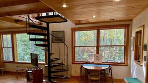 A room with a spiral staircase, large windows, a dining table, and a television. - Tig Foster on Madeline Island (LaPointe)