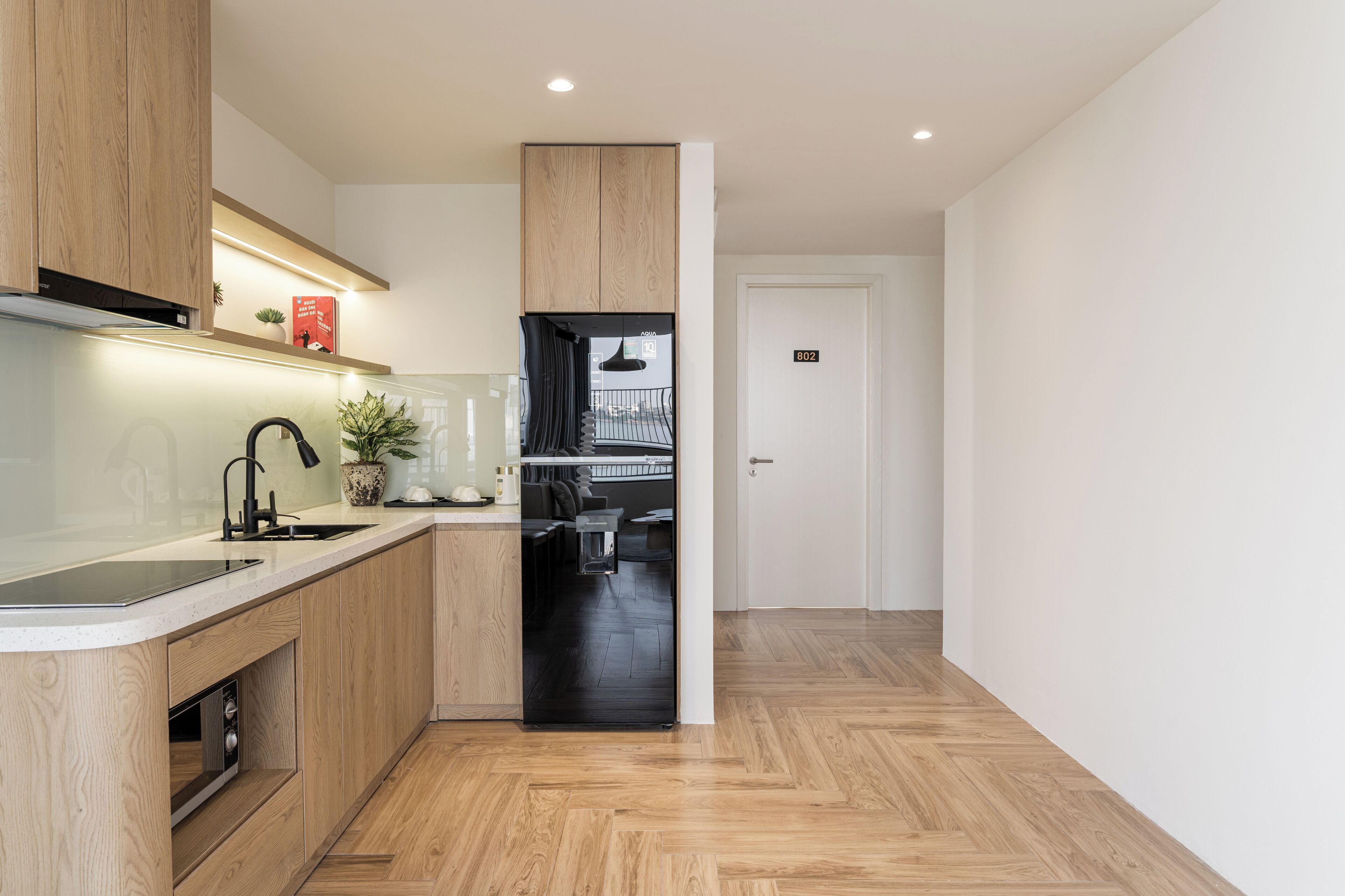 A modern kitchen with wooden cabinets, a black refrigerator, and a built-in oven.