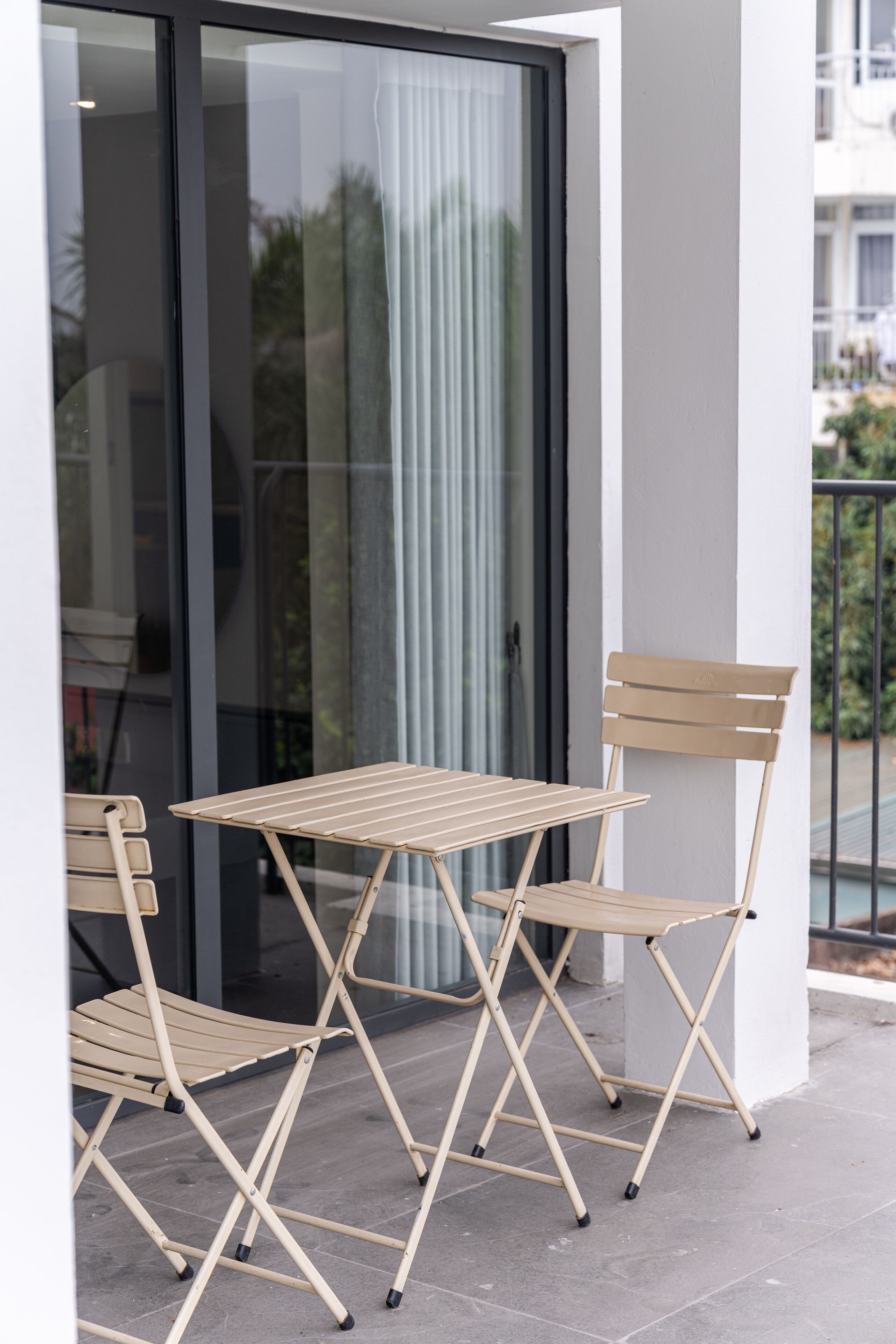 Een balkon met een tafel en stoelen, een glazen deur en een uitzicht op een gebouw op de achtergrond.