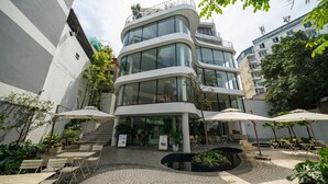 A modern building with a curved facade, outdoor seating area with umbrellas, and a small water feature. - Bach Plateaus Hotel (Hanoi)