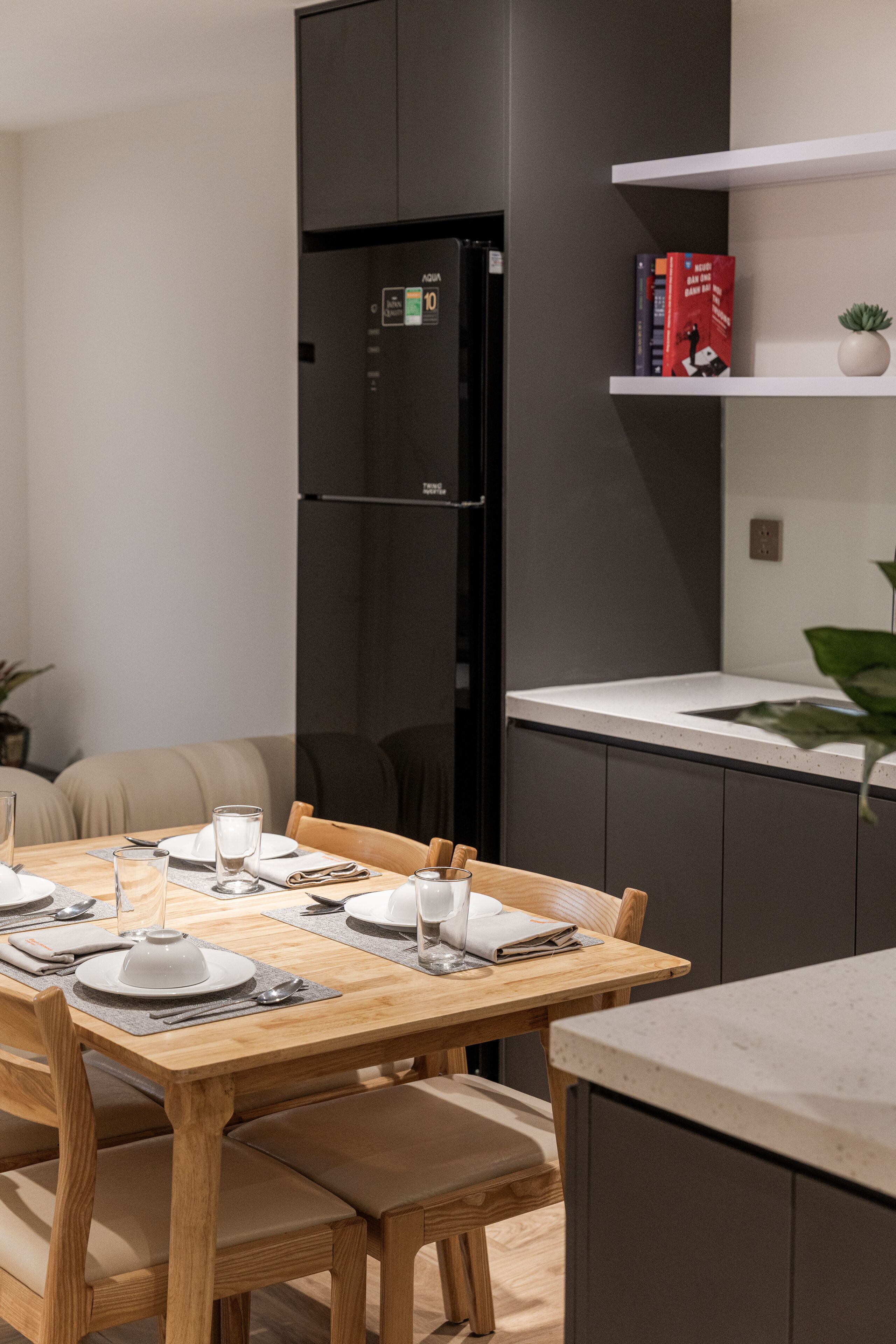 A modern kitchen with a built-in black refrigerator, a wooden dining table set with plates and glasses, and a white countertop.