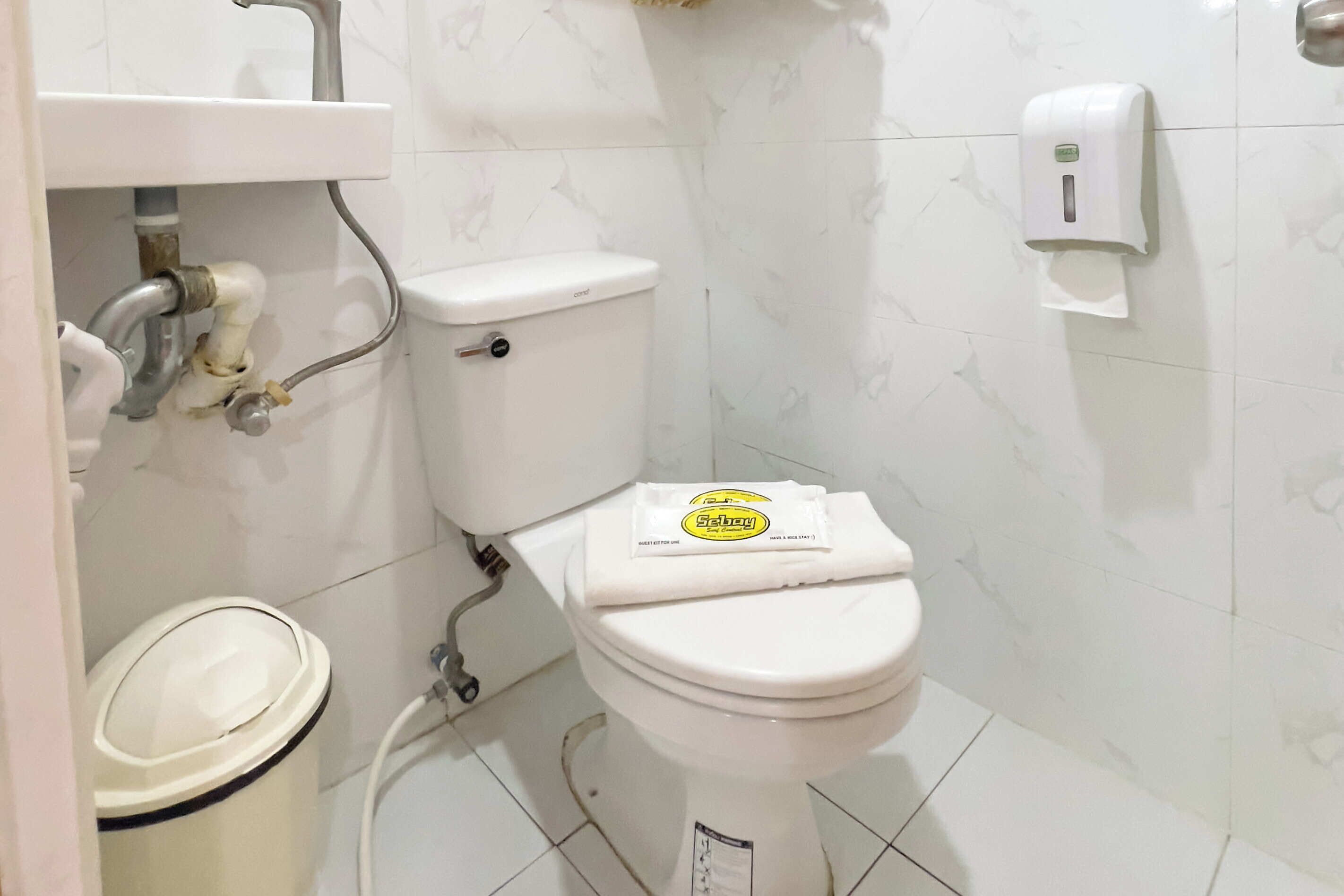 A white toilet with a lid, a hand dryer, and a trash bin.
