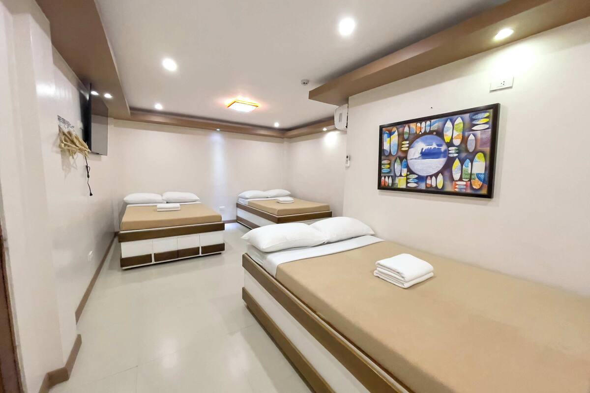 Una habitación de hotel con tres camas, un cuadro en la pared y una lámpara en el techo.