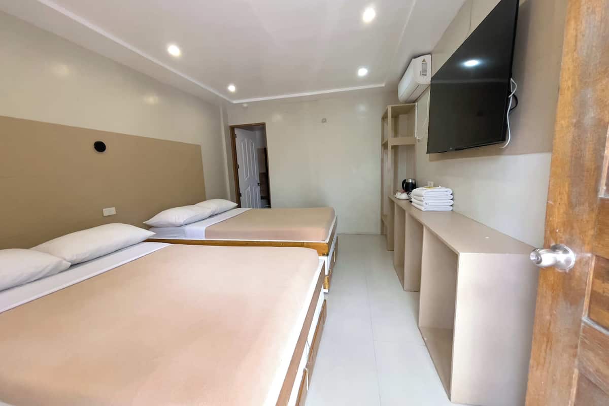 Una habitación de hotel con dos camas, un televisor montado en la pared y una puerta de madera.